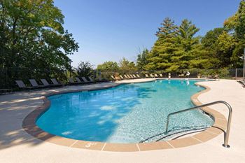 A swimming pool surrounded by trees and lounge chairs.