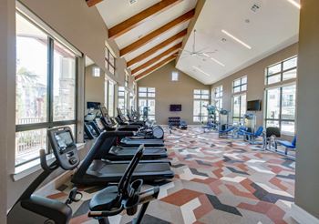 a gym with cardio equipment and large windows