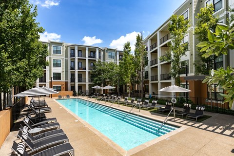 A swimming pool surrounded by lounge chairs and umbrellas in front of apartment buildings.