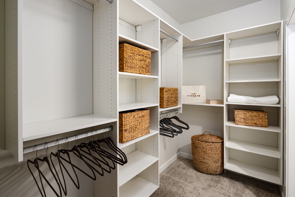 a walk in closet with white shelving and wicker baskets