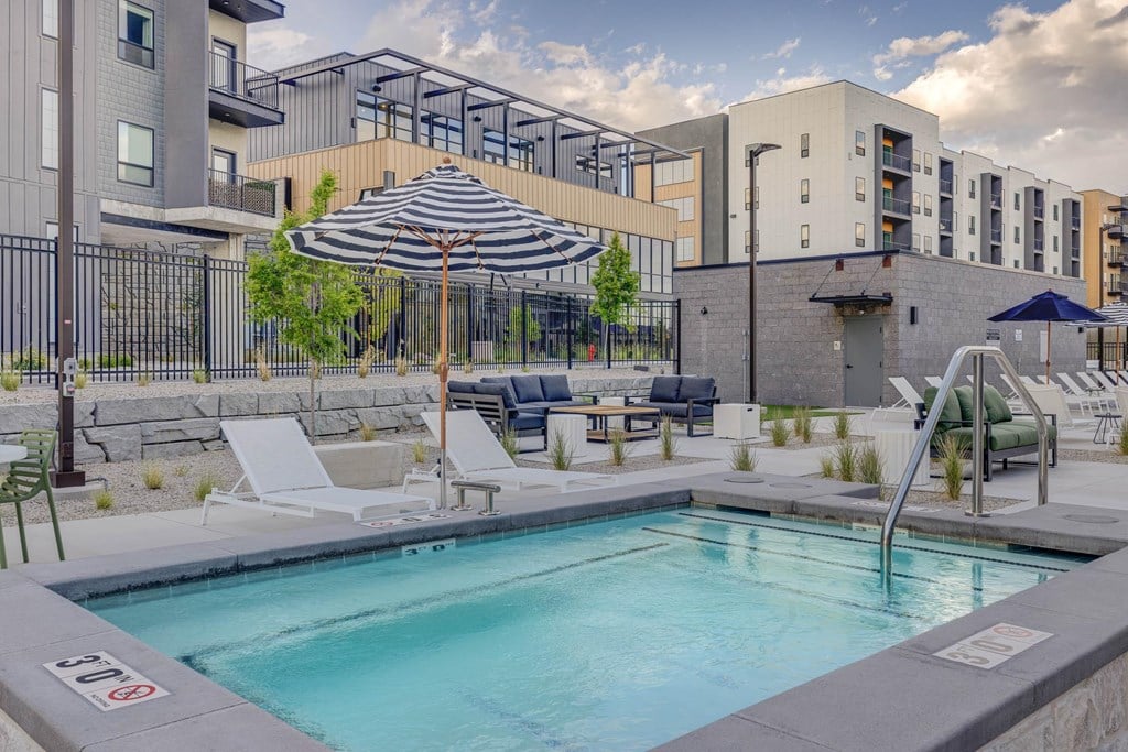 A pool surrounded by a patio with chairs and umbrellas.