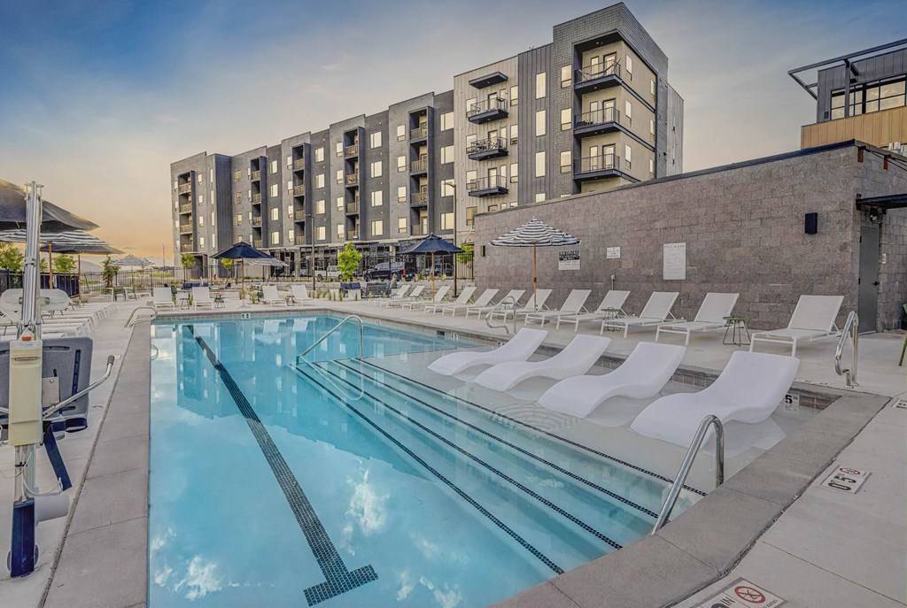 A swimming pool with lounge chairs and apartment buildings in the background.