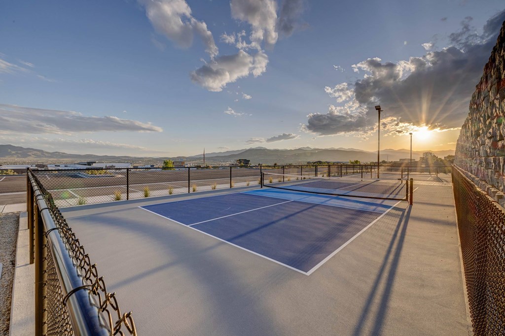 A tennis court with a fence and a sunset in the background.