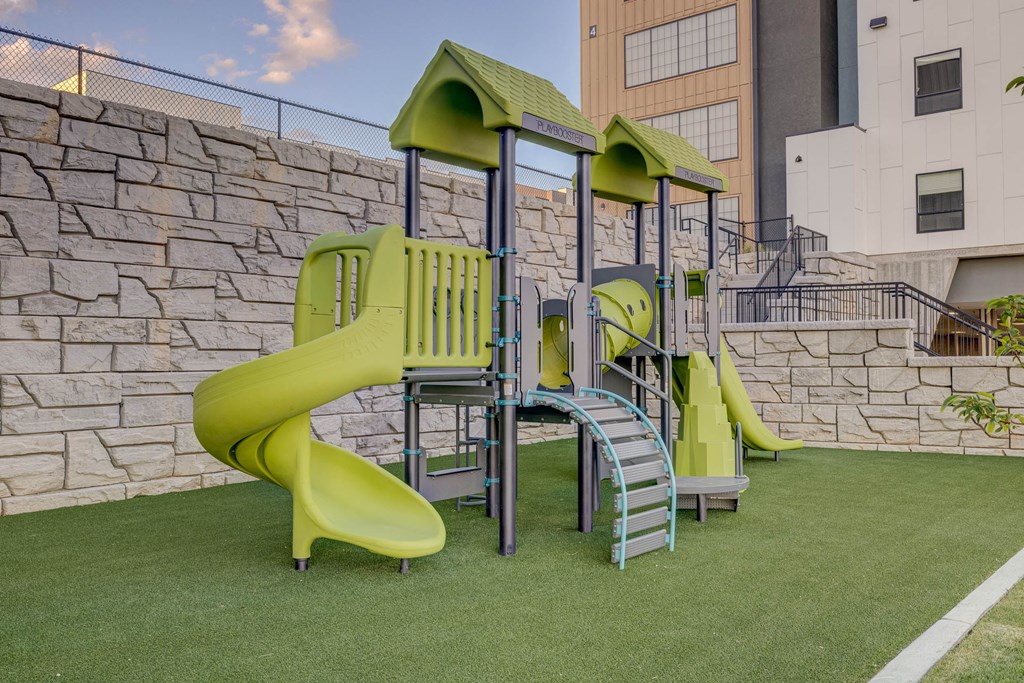 A playground with a green slide and a grey and green play structure.