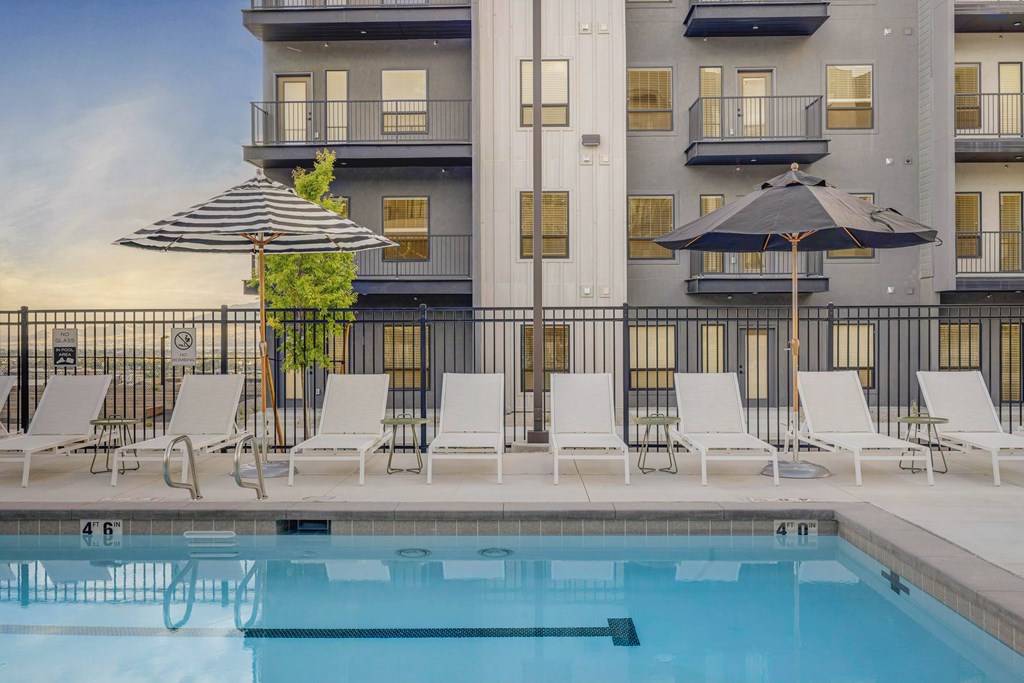 A pool area with lounge chairs and umbrellas in front of a building.