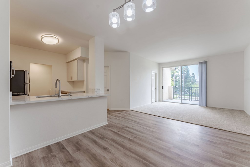 A spacious, empty room with a kitchen area and a door leading to a balcony.