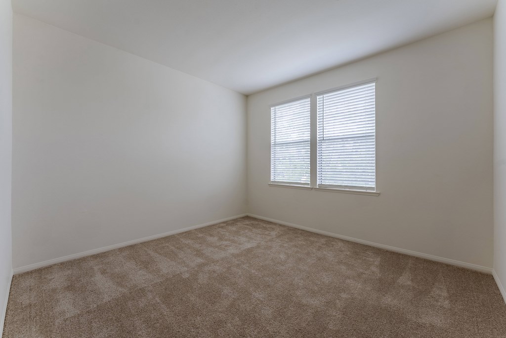 A room with a carpeted floor and a window with blinds.