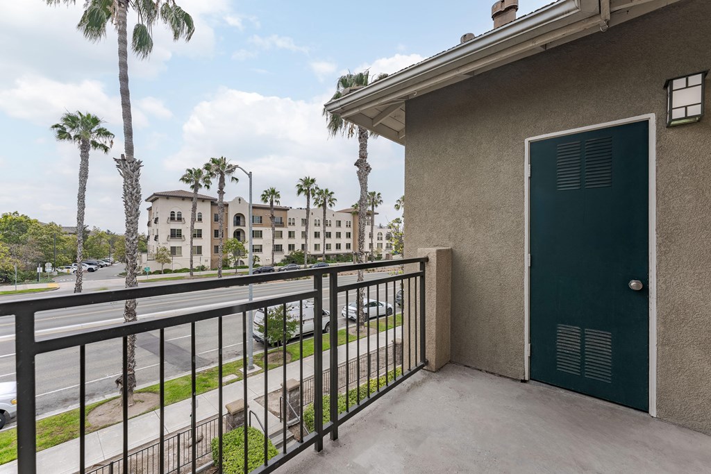 A balcony with a green door and a black railing overlooks a street with palm trees.