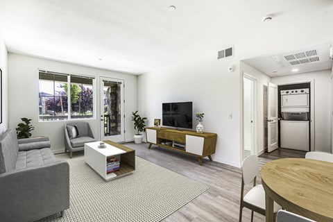 A living room with a grey couch, a white coffee table, a television, and a dining table.