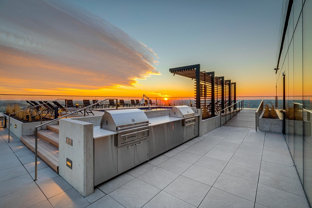 a terrace with two barbecue grills and a sunset over the ocean
