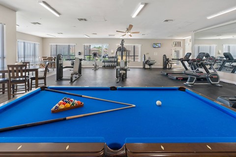 A pool table with a pool ball and cue sticks in the foreground and a gym in the background.