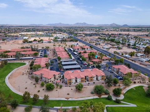 A large building with a red roof is surrounded by a parking lot and other buildings.