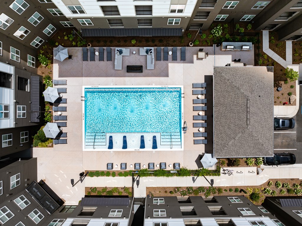A swimming pool surrounded by lounge chairs and umbrellas in a courtyard.