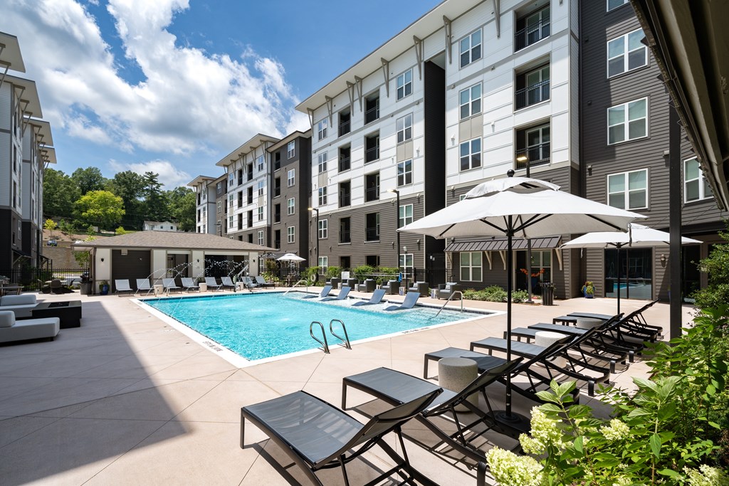 A pool area with sun loungers and umbrellas in front of a building.
