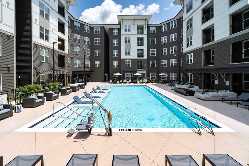 A large swimming pool surrounded by lounge chairs in front of apartment buildings.