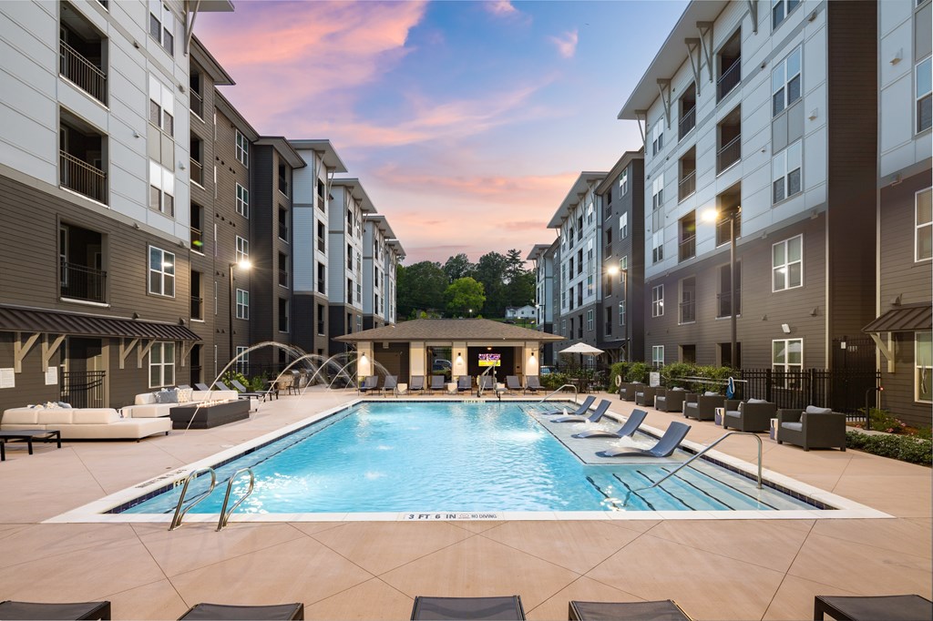 A large swimming pool surrounded by lounge chairs and apartment buildings.