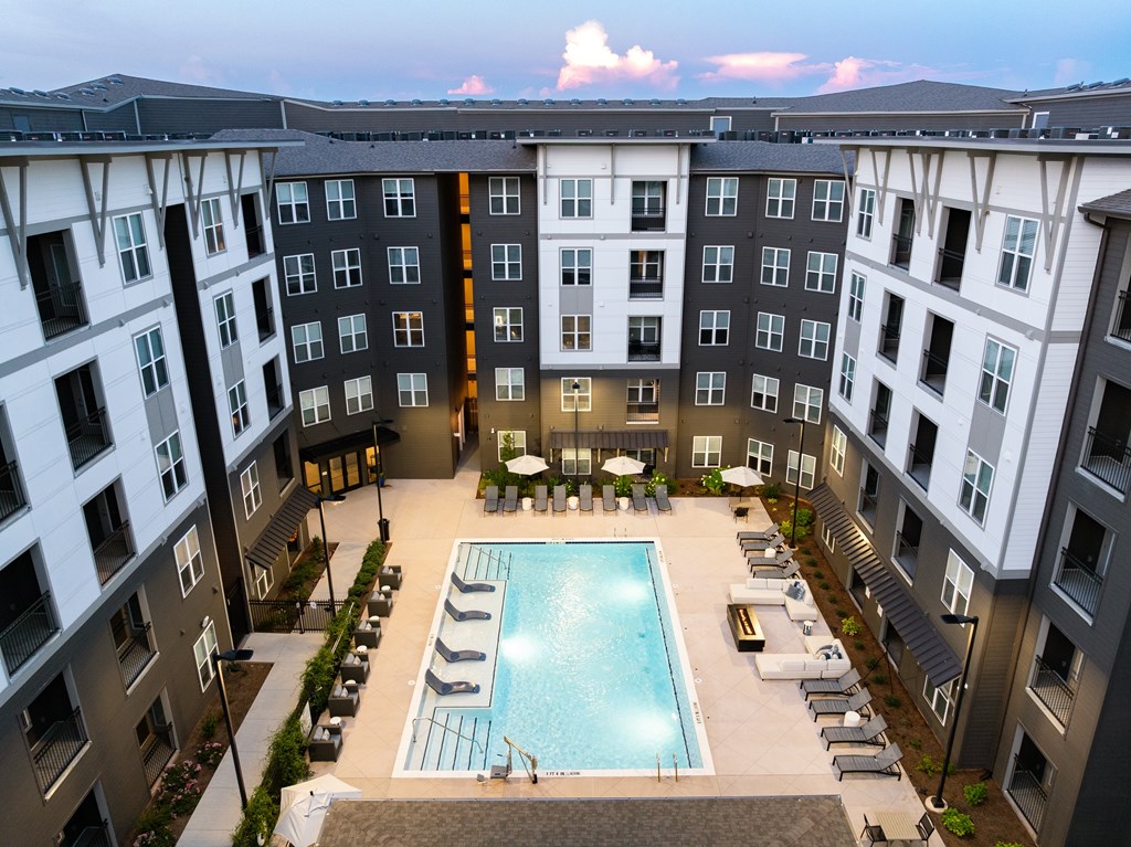 A large swimming pool is surrounded by lounge chairs in the courtyard of apartment buildings.