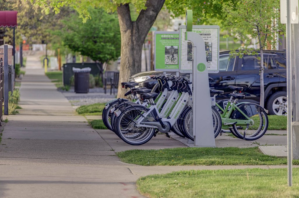a row of green-bikes parked on the sidewalk near our apartment community