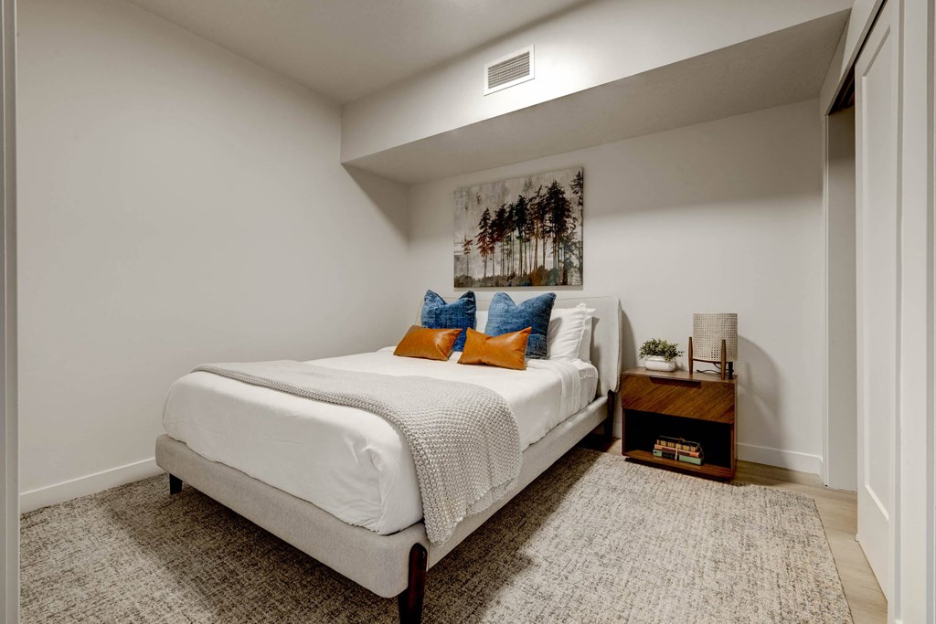 bedroom with white walls and a white bed with orange and blue pillows