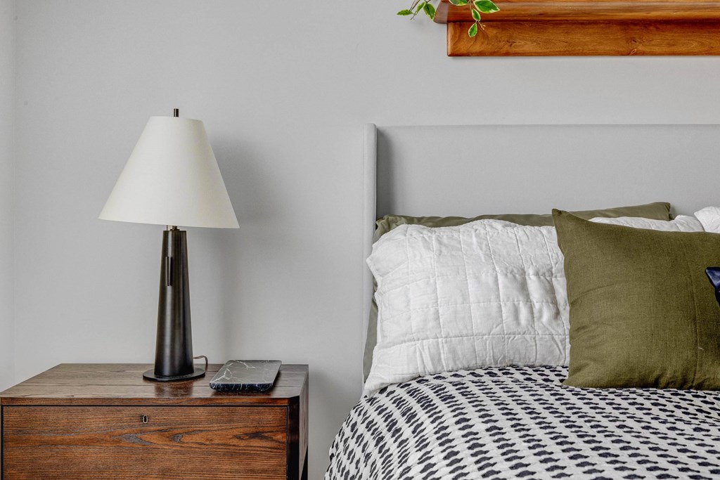A bed with a white pillow and a green pillow is next to a lamp on a nightstand.
