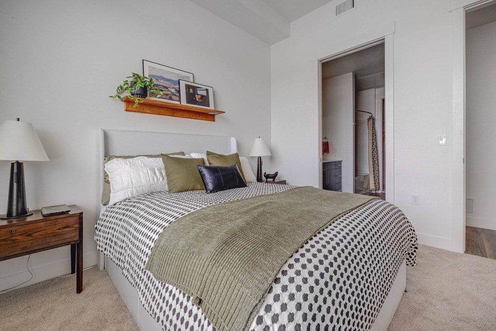 A bedroom with a large bed and a lamp on a side table.