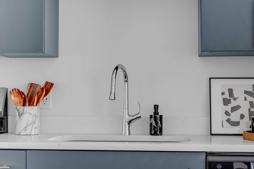 A kitchen sink with a faucet and a cup of spoons.