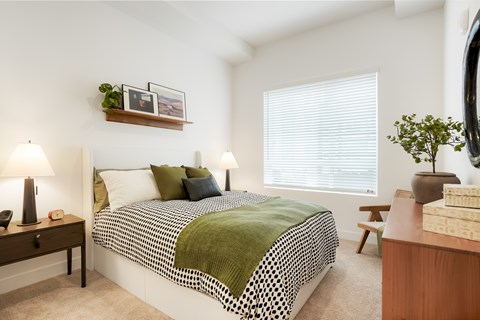 A bedroom with a bed, nightstand, and a window with blinds.