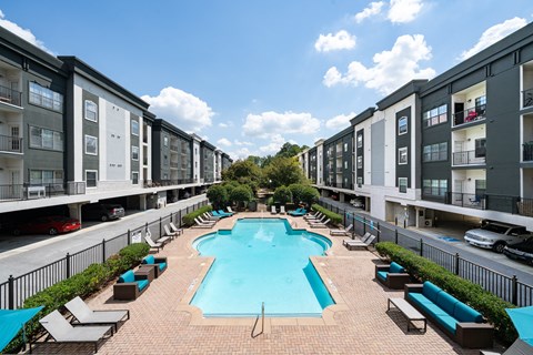 A swimming pool surrounded by lounge chairs and apartment buildings.
