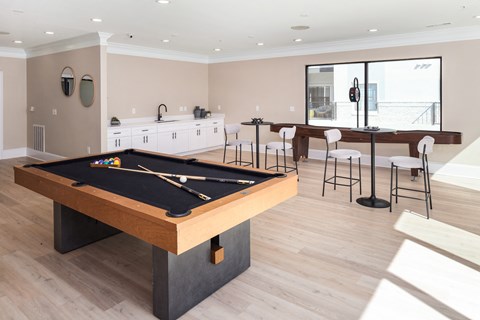 A pool table is in the middle of a room with a bar and stools.
