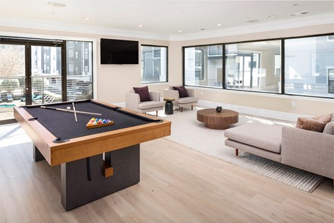 A pool table is in the middle of a living room with a couch and a TV.