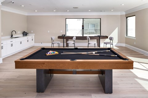 A pool table is in the middle of a room with a kitchen in the background.