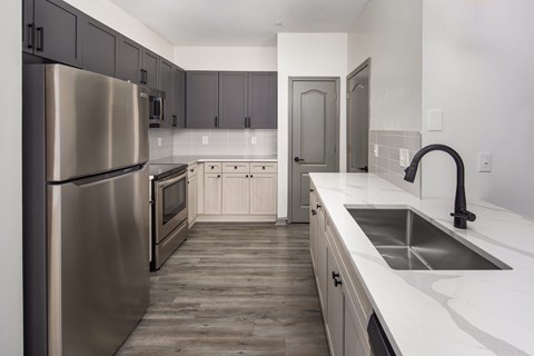 A modern kitchen with a stainless steel refrigerator and wooden flooring.