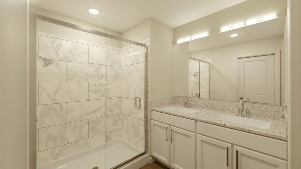 A bathroom with a marble tile shower and white cabinetry.
