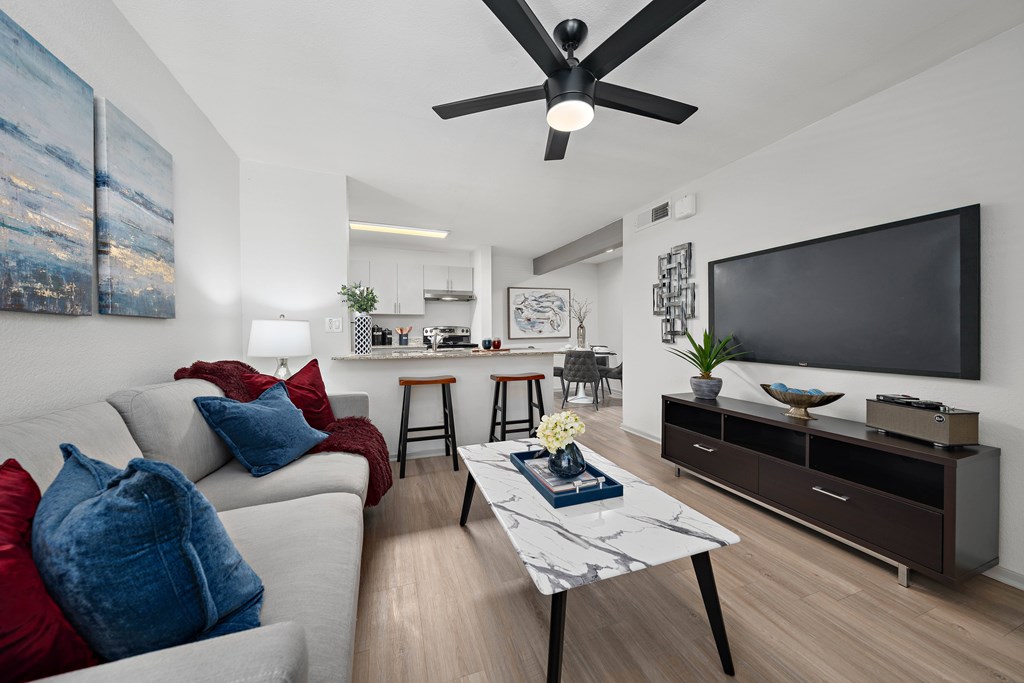 A modern living room with a grey sofa, a white coffee table, and a black ceiling fan.