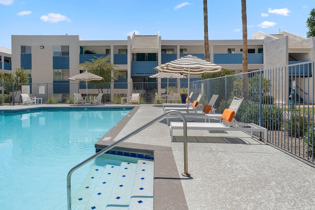 Pool with lounge chairs and striped umbrellas at The Halifax apartments in Phoenix, AZ.