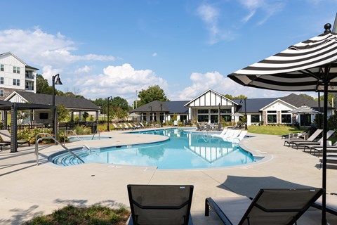 A pool area with chairs and umbrellas in front of a building.