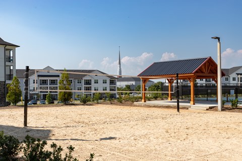 A sandy area with a building in the background and a wooden pavilion in the foreground.