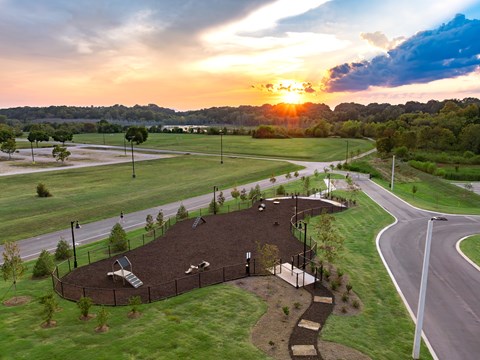 A playground with a slide and a basketball court is surrounded by a fence and trees.