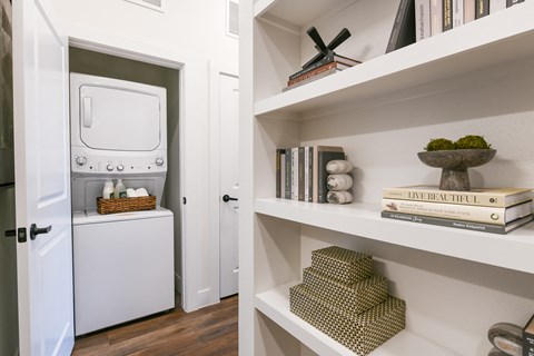 a white washer and dryer in a room with white shelves and a door