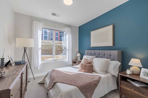 A bedroom with a bed, nightstand, and a window with a view of a building outside.
