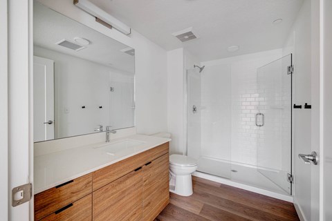 A white bathroom with a wooden vanity and a walk-in shower.