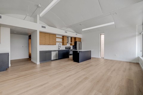 A spacious room with wooden floors and a kitchen area with a sink and stove.