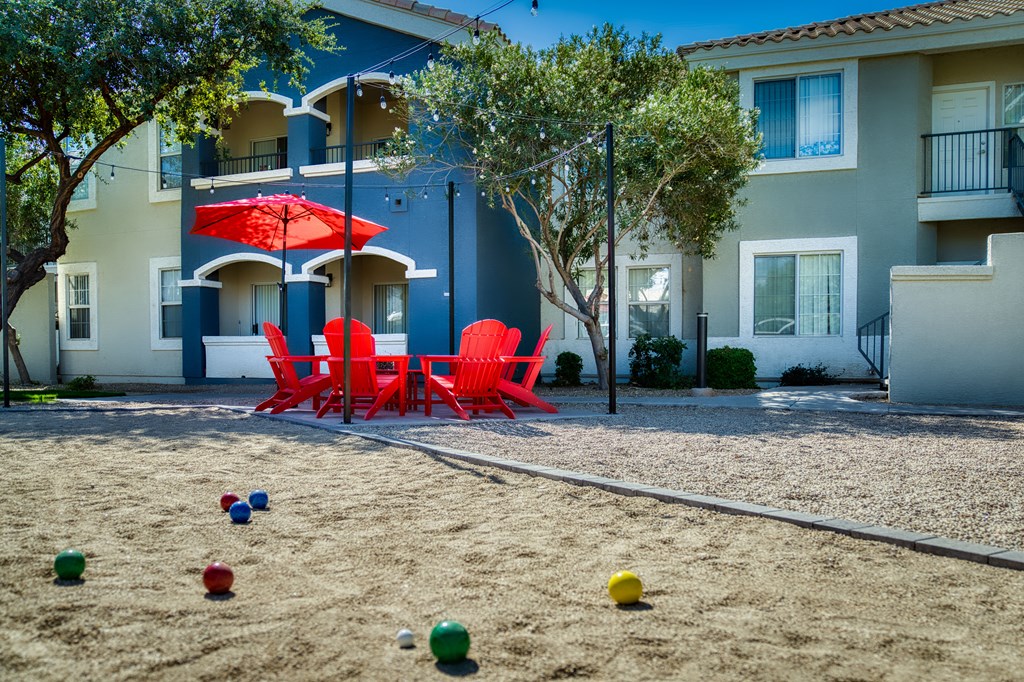 a playground with red chairs and umbrellas in front of an apartment building