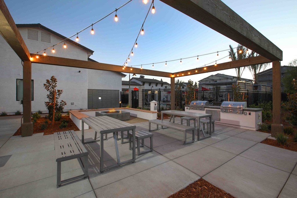 a patio with tables and benches and string lights