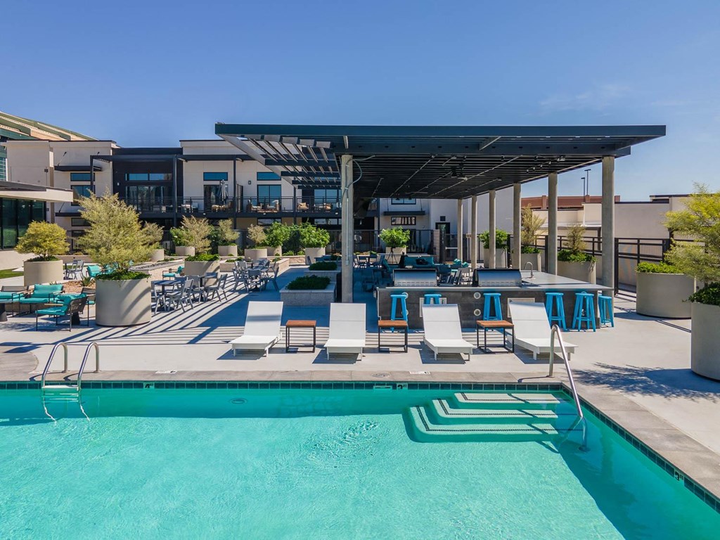 a pool with lounge chairs and a shade structure at an apartment complex