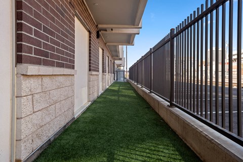 a grass covered walkway between a brick building and a metal fence