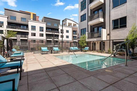 an apartment swimming pool with lounge chairs and buildings in the background