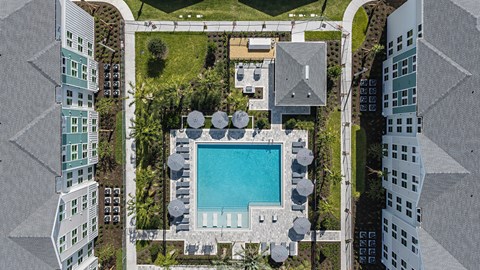 A swimming pool surrounded by lounge chairs and umbrellas in the middle of a grassy area.