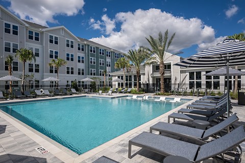 A large swimming pool surrounded by sun loungers and umbrellas in front of a hotel.