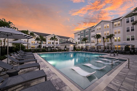 A swimming pool surrounded by lounge chairs and umbrellas in front of a building.
